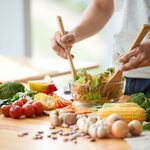 Photo: A man mixing a salad filled with green vegetables in a clear, glass bowl