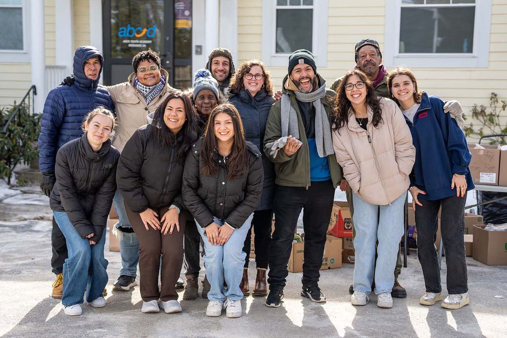 Photo: A group of people smiling and posing while wearing winter jackets outside of a building