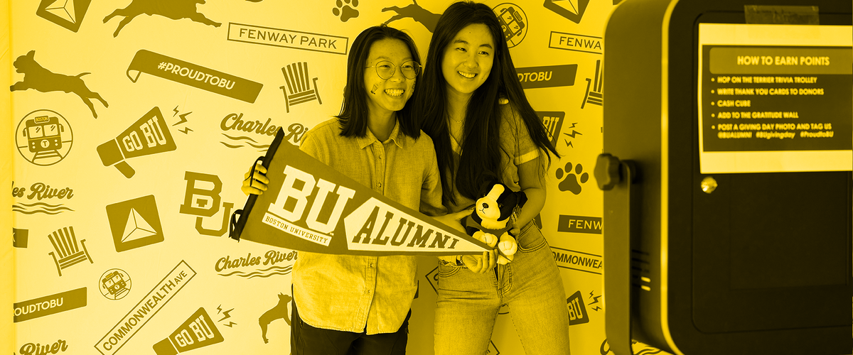 2 women holding a BU Alumni flag