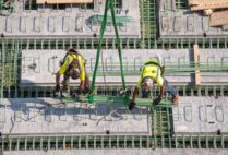 two construction workers balance on a sea of green pegs