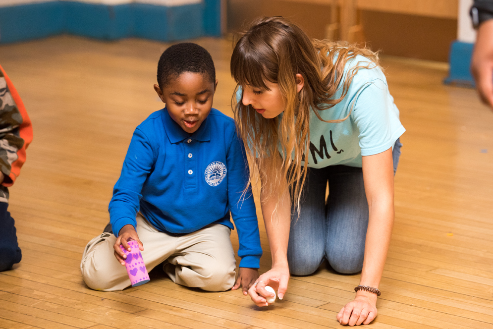 A student kneels next to a five-year-old and talks with him