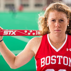 Portrait of Ally Hammel, Boston University Terriers field hockey NFHCA All-American, wearing her BU jersey and holding her stick on her shoulders.