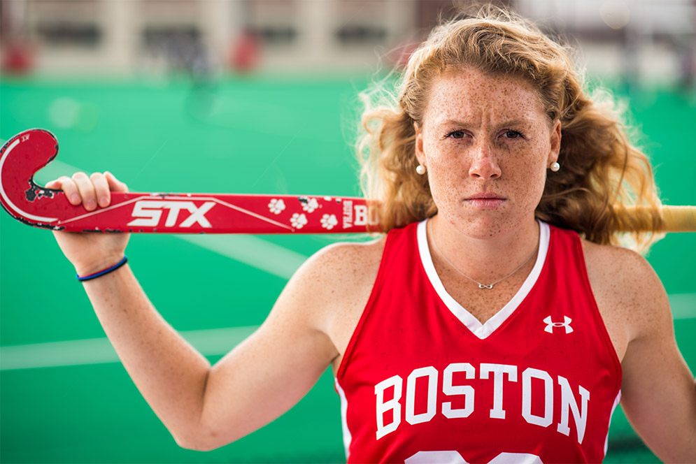 Portrait of Ally Hammel, Boston University Terriers field hockey NFHCA All-American, wearing her BU jersey and holding her stick on her shoulders.