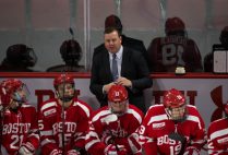 BU men's ice hockey head coach Albie O'Connell talks to a player on the bench during a game.