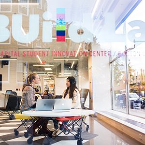 A BU student works with her Hub cocurricular supervisor, seen through the window of the BUildLab: IDG Capital Student Innovation Center at Boston University.