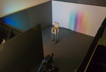 A rainbow penumbra on a far wall is created by a bright scene displayed on an LCD monitor (left) and a chair (center).