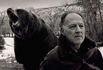 Werner Herzog with a grizzly bear roaring behind him, in grayscale