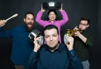 Boston University Ph. D. candidate Reza Ghaffarivardavagh poses with his research team. Reza holds the noise cancellation devices his team developed over his ears while his teammates make noise banging a pot, playing a trumpet, and a boombox in the background