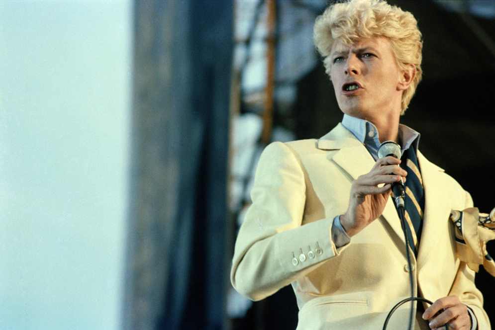 David Bowie wearing a yellow suit and holding a microphone at a concert