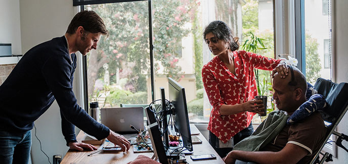 Craig Cloutier speaks to Rahul Desikan while Maya Vijayaraghavan helps Desikan sip a drink.