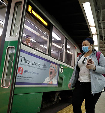 Woman wearing a mask and holding a phone while boarding a green line train