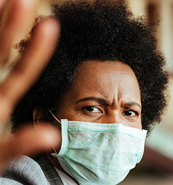 A woman wearing a mask putting her hand up to prevent someone from coming too close