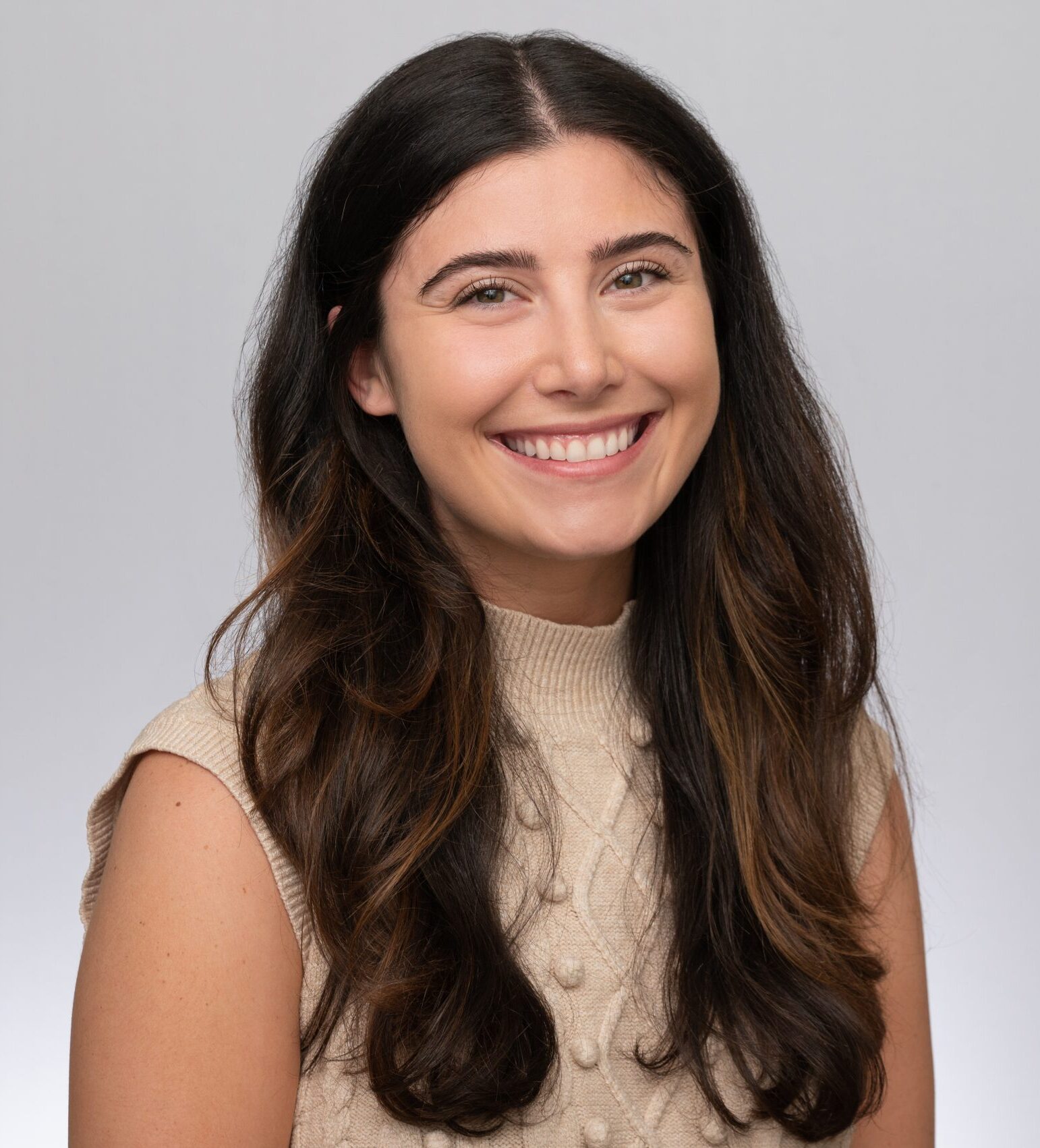 Danielle is wearing a cream colored sweater vest and her hair down in this headshot