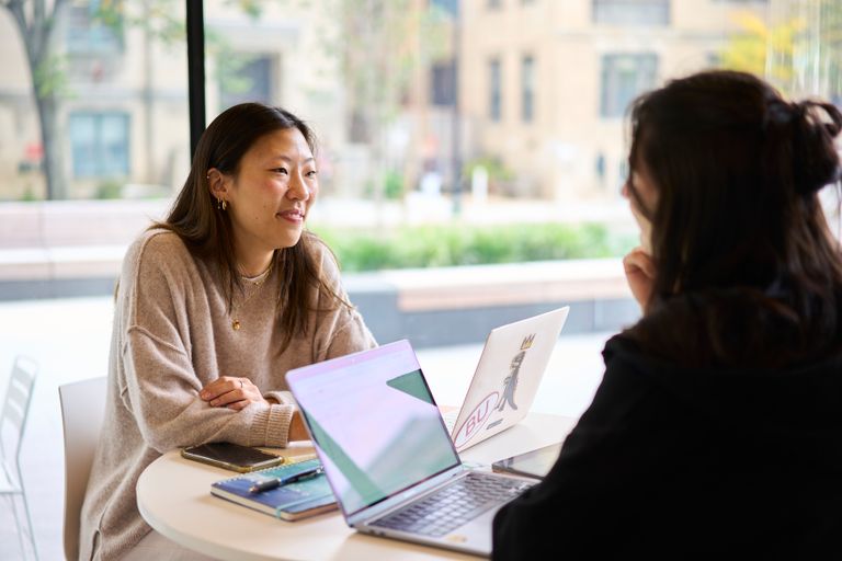 Photo of two students sitting at a table working together on laptops.
