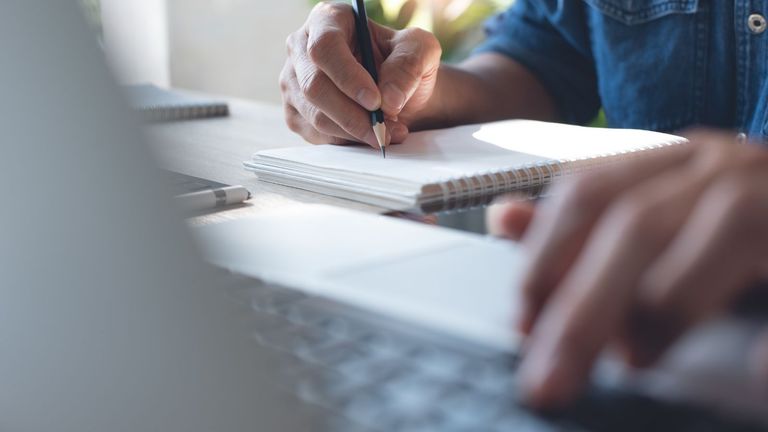 Photo of person's hands as they use a laptop and write notes