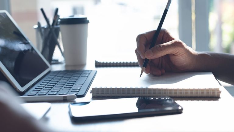 Photo of a person's hand taking notes in front of a laptop