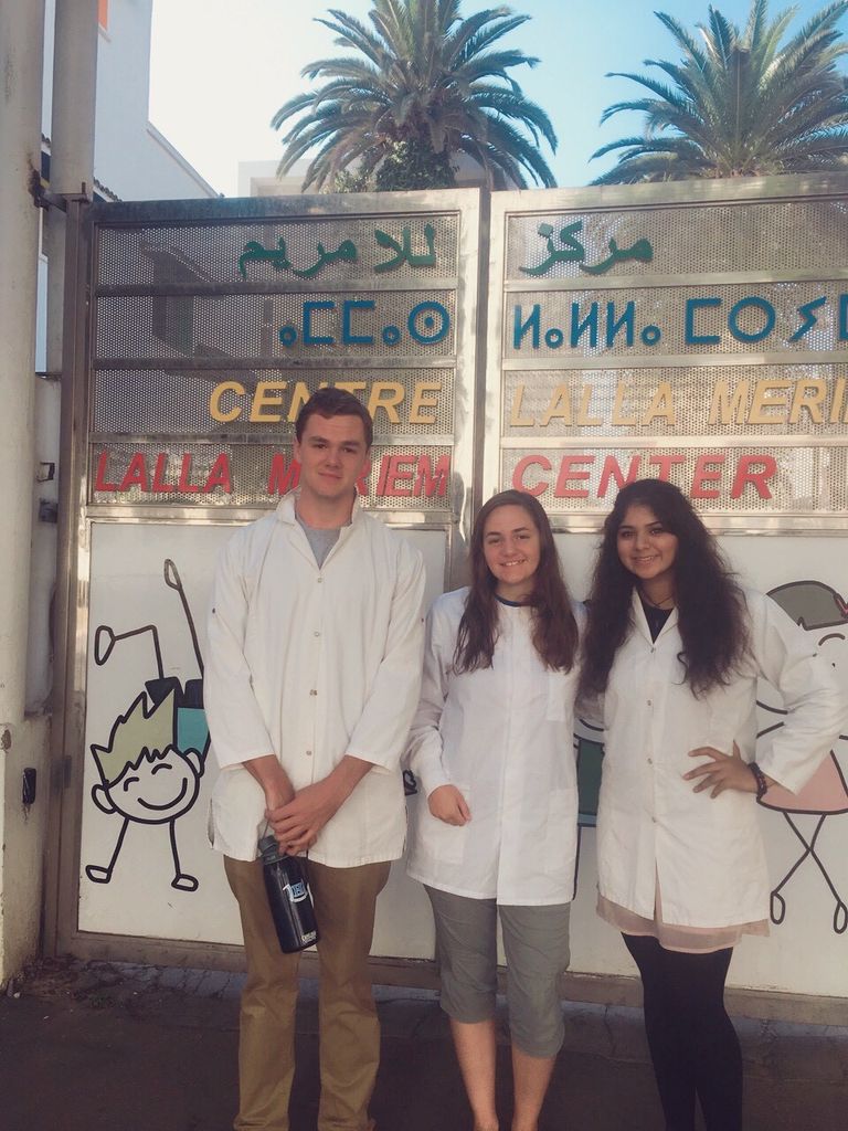 Aisha Sheikh and two other friends, wearing white coats and standing in front of the orphanage