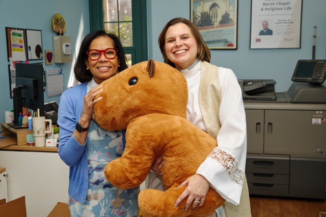 Rev. Karen and Rev. Jessica smile at the camera in the 马什教堂 office while holding a large capybara stuffed animal