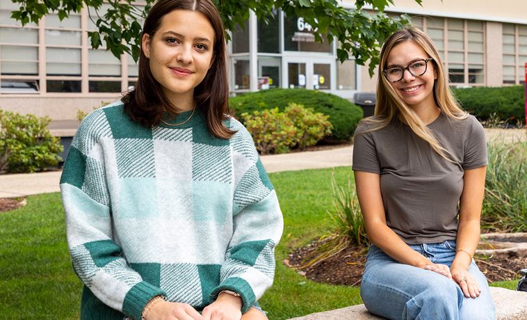 Two female students seated on the COM lawn.