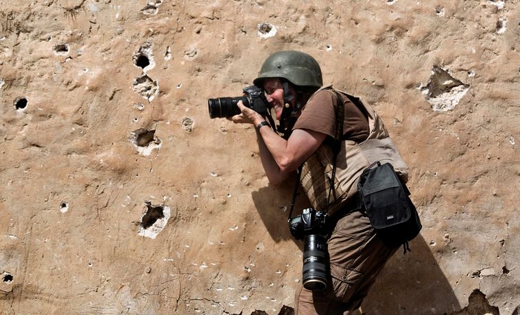 Carol Guzy taking photos while dressed in fatigues and wearing a helmet