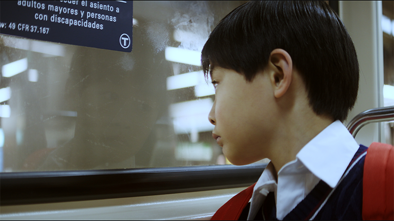 Production still from Bob, showing a young Asian boy peering out a subway car window.