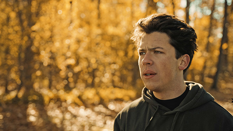 Production still from Runner's Blood, showing a young man wearing a hoodie with woods in the background.