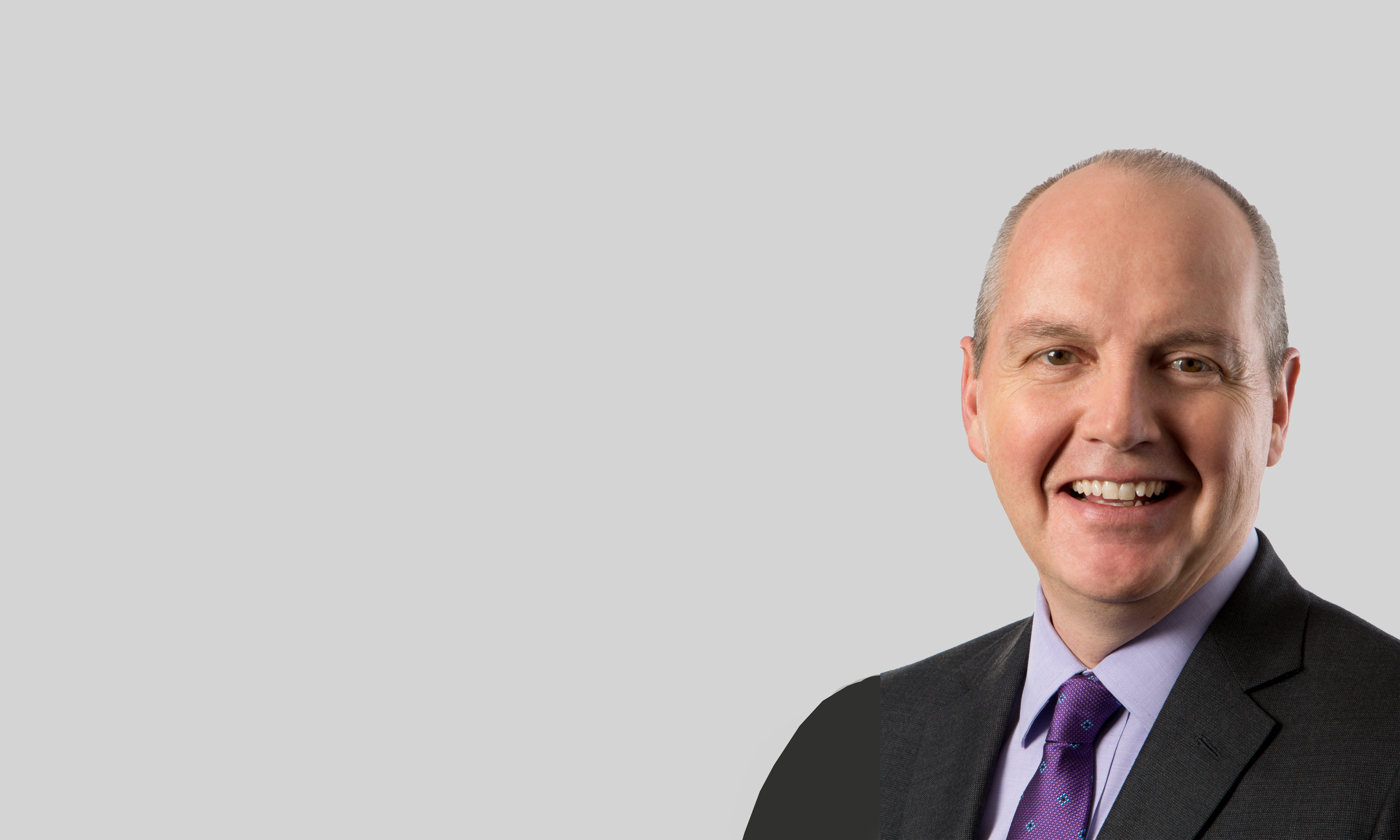 White man smiling at camera, wearing suit and purple tie.