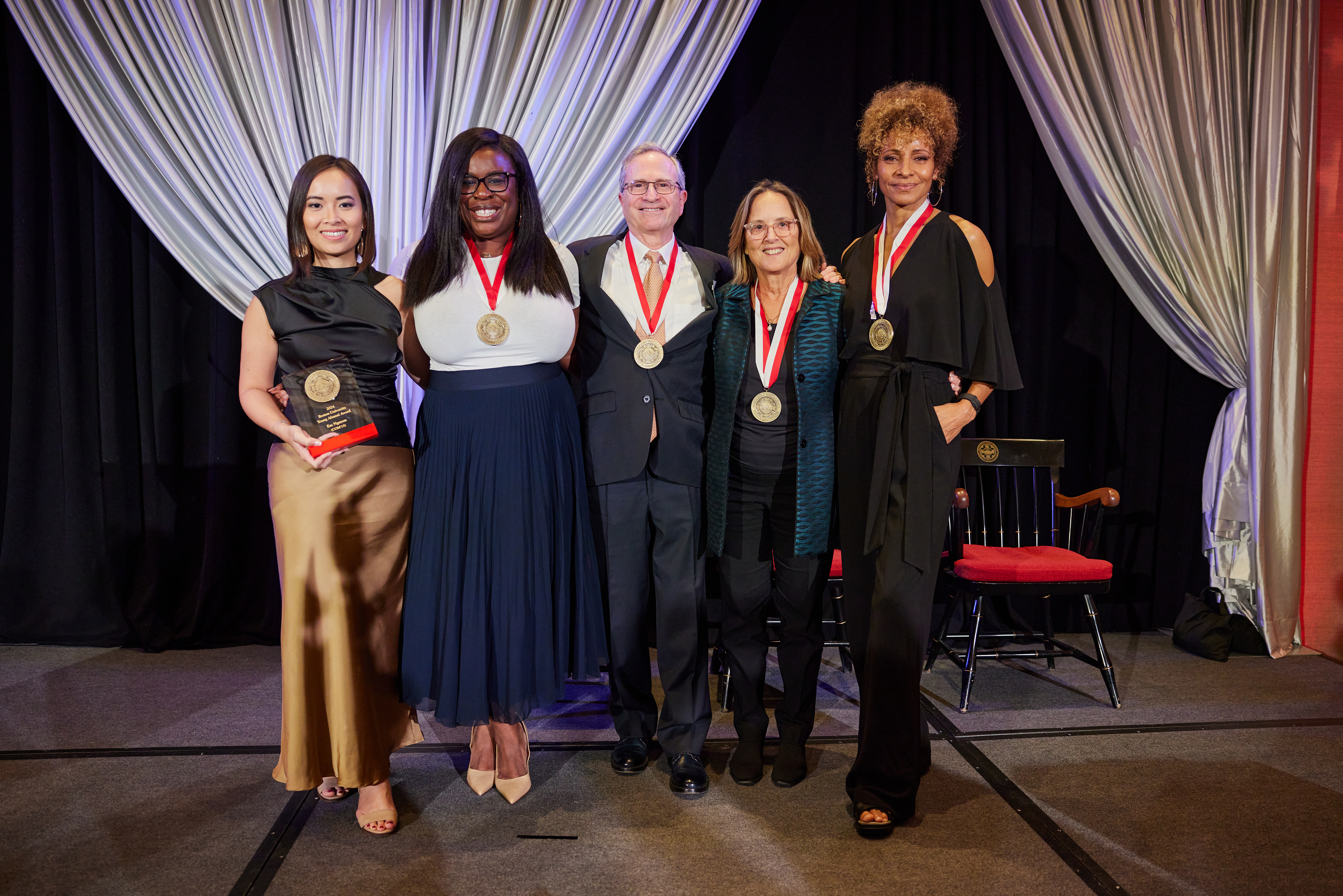 Four women and one man with gold medals stand on a stage.
