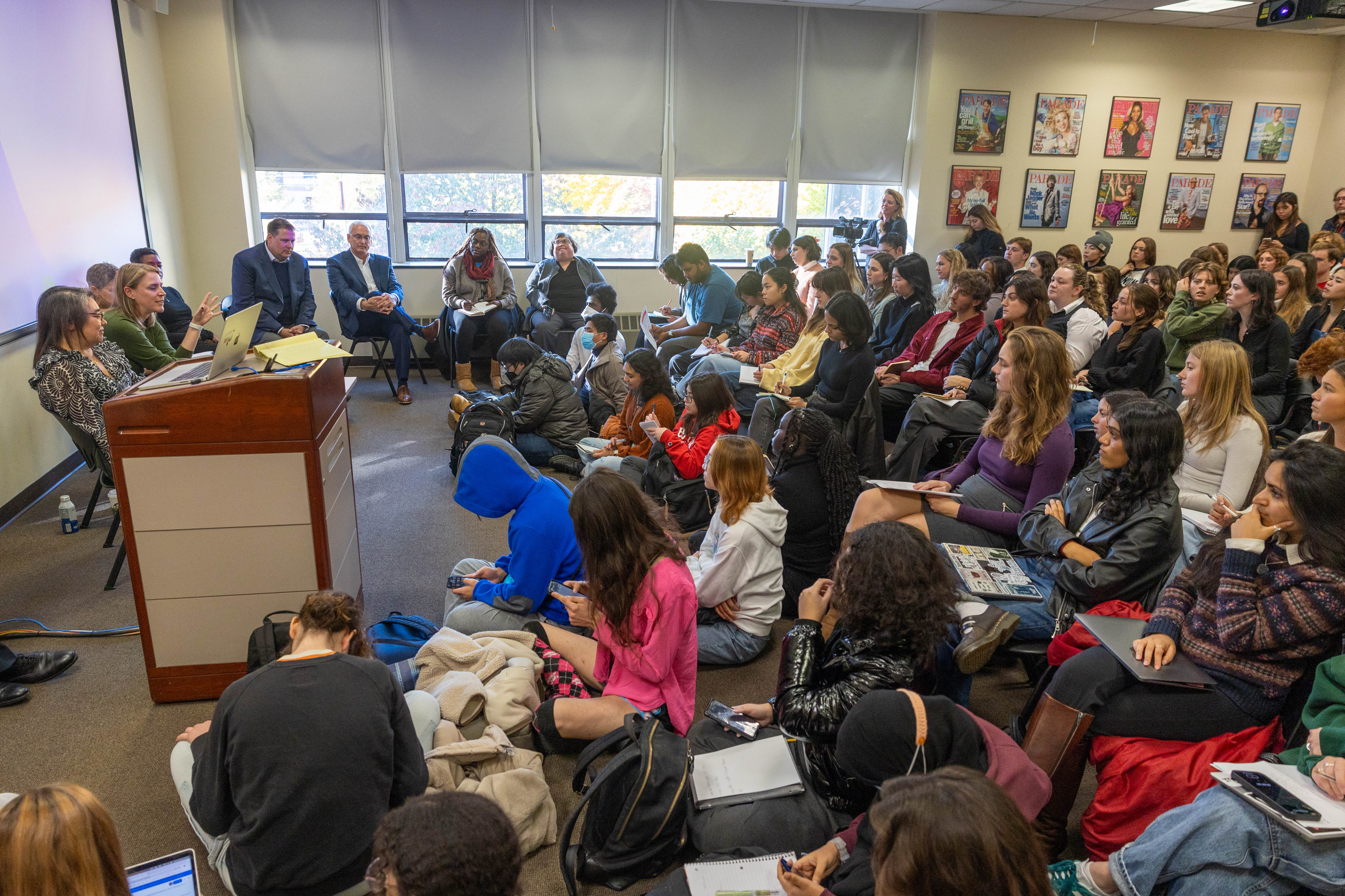A large group of students listening to a panel of speakers in a classroom.