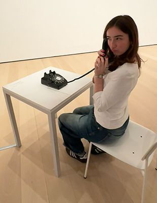 Carly sitting at white table holding rotary phone