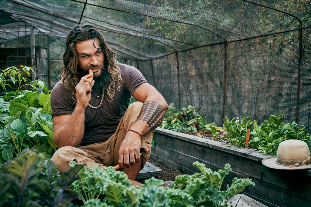 Jason Momoa eating a carrot in a greenhouse