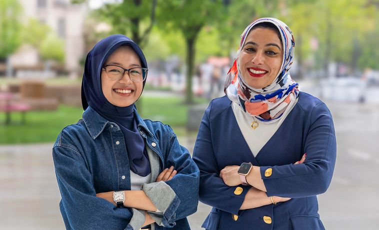 Two women, wearing head coverings, pose with their arms crossed.