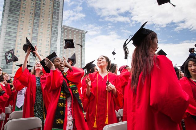 Crowd of BU graduates in red gowns tossing their black mortarboard caps in the air.