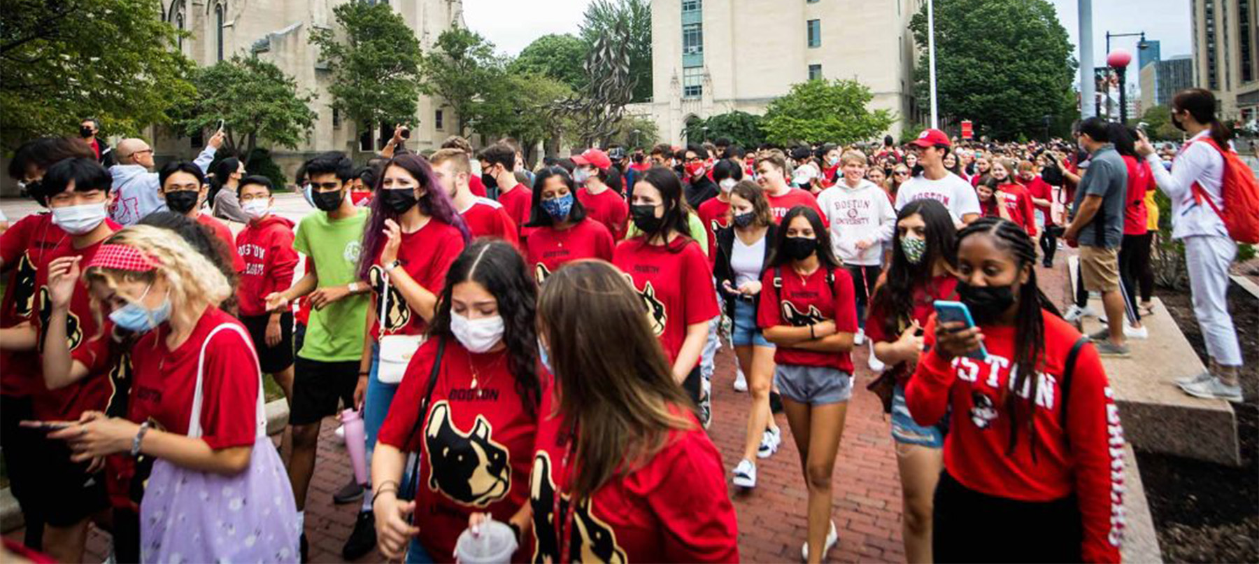 Groups of students, many in red BU shirts, marching in front of Marsh Plaza on their way to Matriculation at Agganis Arena.
