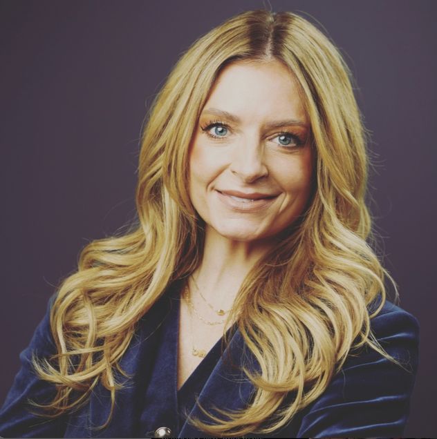 Picture of Nedra, a smiling oman with long dirty-blonde hair. She is wearing a blue suit and her head is slightly tilted.