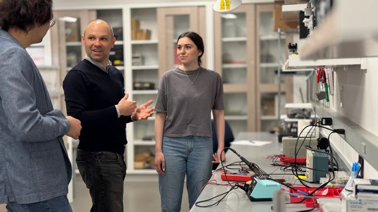 Three people standing in a lab, to test some hardware they create to study human brain functions