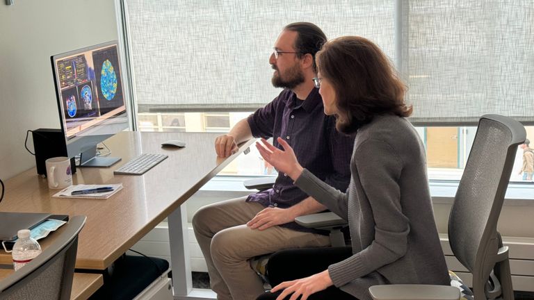Two people sitting in front of a computer to examine a data visualization from a functional magnetic resonance imaging