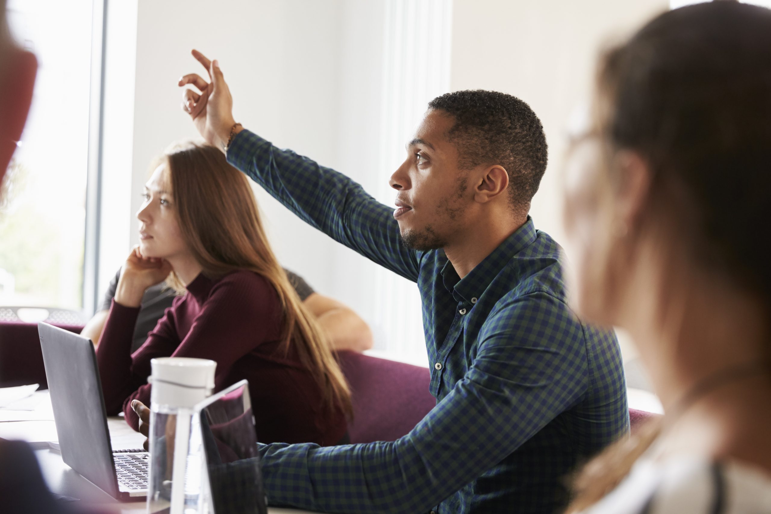 black male student raising hand and a white female student sitting to him view from the side