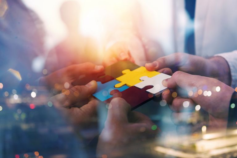 people holding together different colored puzzle pieces with their hands, the puzzle suspended in the air