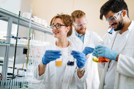 three students working in a STEM lab to complete an experiment. Two students in the front are holding test tubes and one student in the back is recording data.