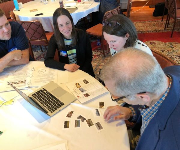 a group of people sit around a white table analyzing images