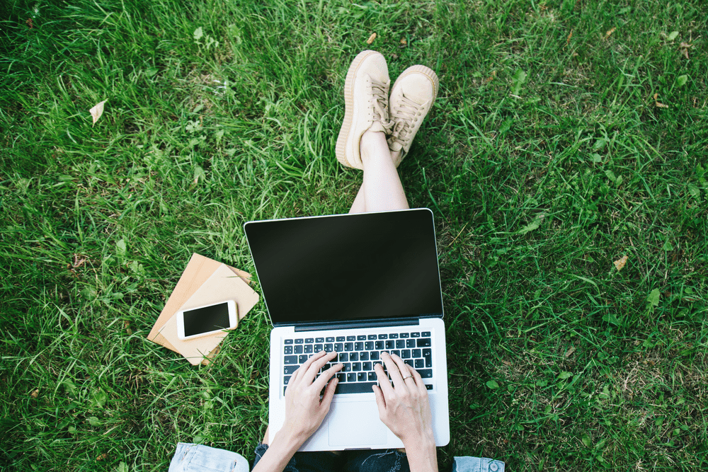 Person with legs crossed, using a laptop outside on the grass