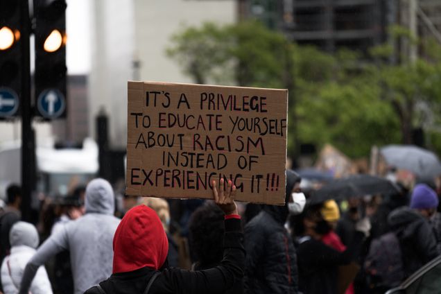 Protestor holding sign: "It's a privilege to educate yourself about racism instead of experiencing it!!!"