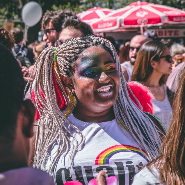 Photo of a Black woman in crowd at LGBQTIA+ pride event decorated in rainbows
