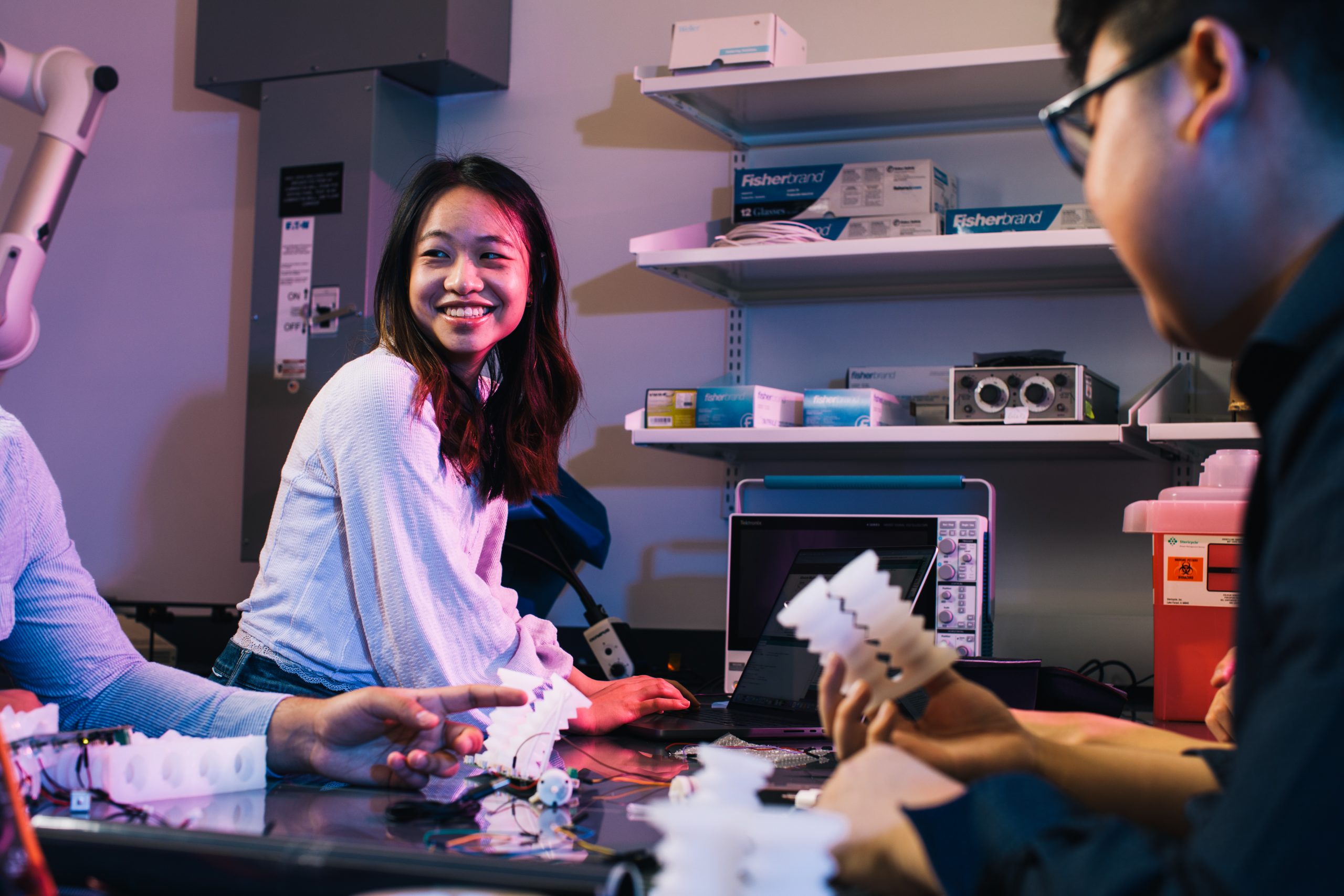 Female engineering student smiling as she works with other students in a lab setting
