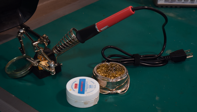 soldering iron with a red handle with helping hands, a fume vent, a tip cleaning vessel, and a flux container around it