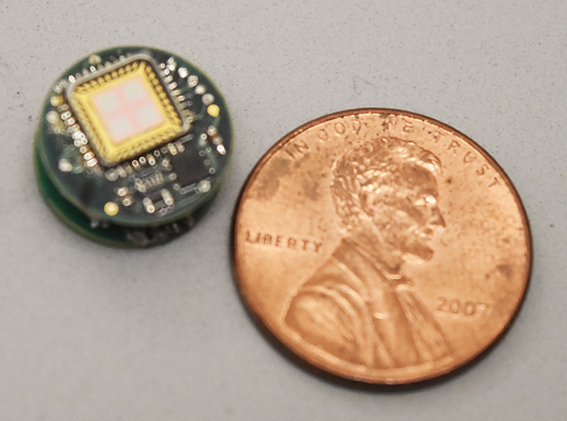 Photo shows a tiny device made of layered microchips, with a penny for scale.