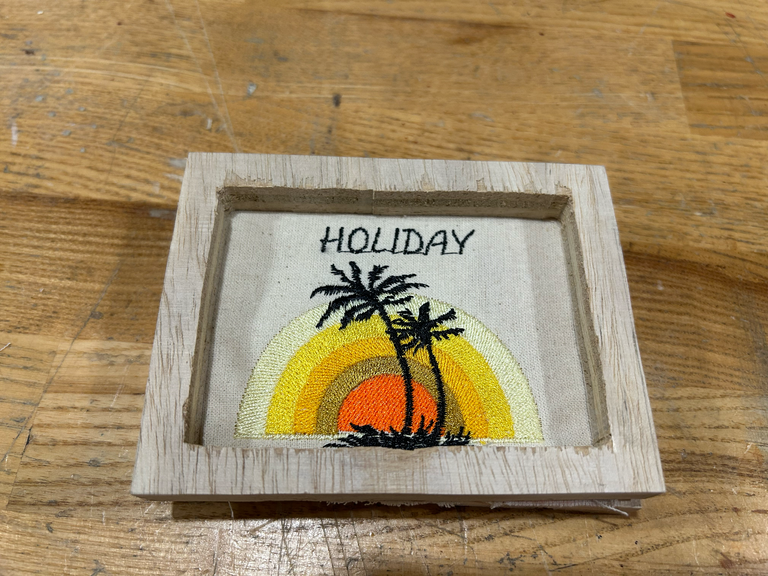 small wooden frame with an embroidered image of a sunset with palm trees in the middle