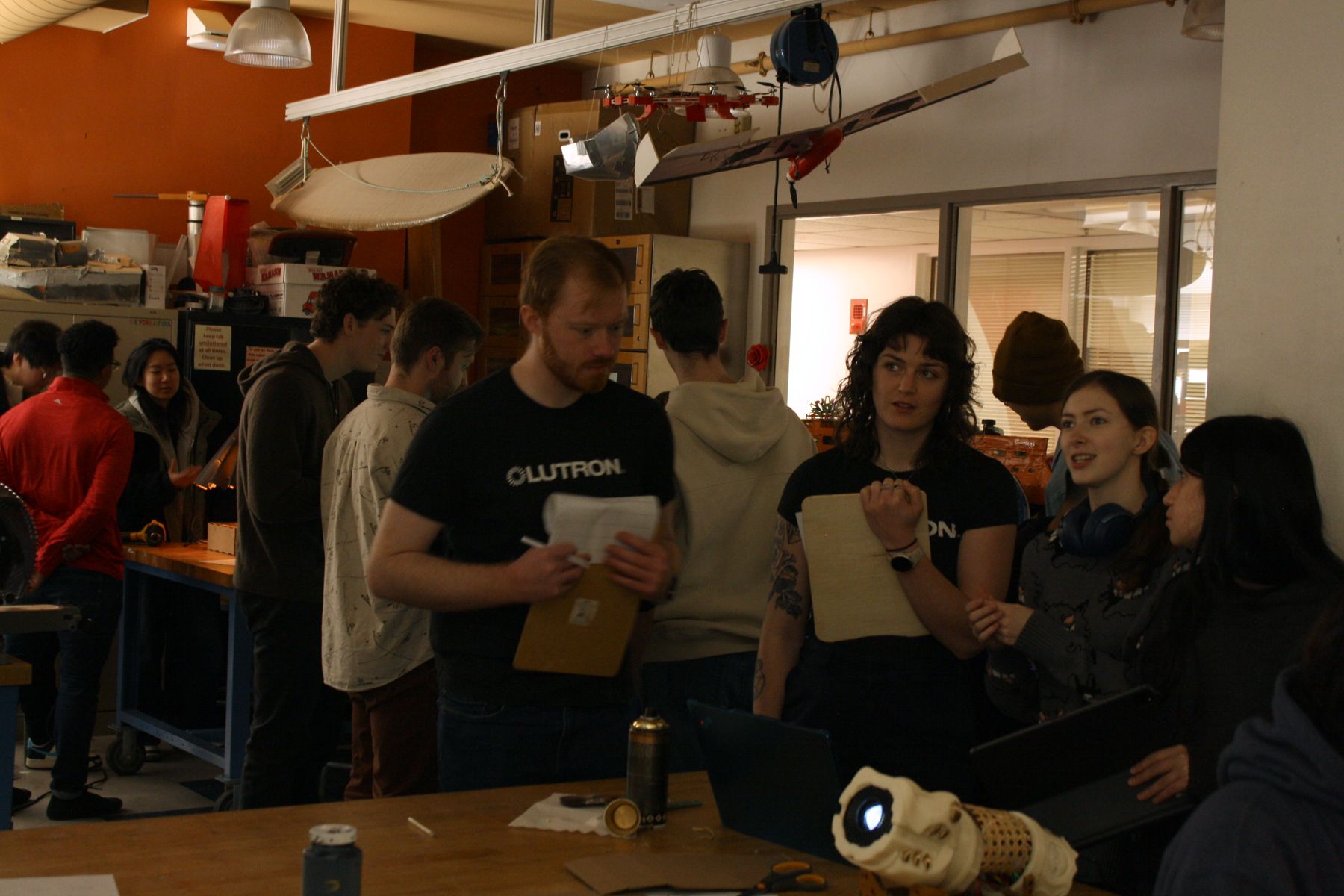 wide group shot showing the 2 students showing off their dragon shaped proejctor to the lutron judges while more competition activity happens behind them