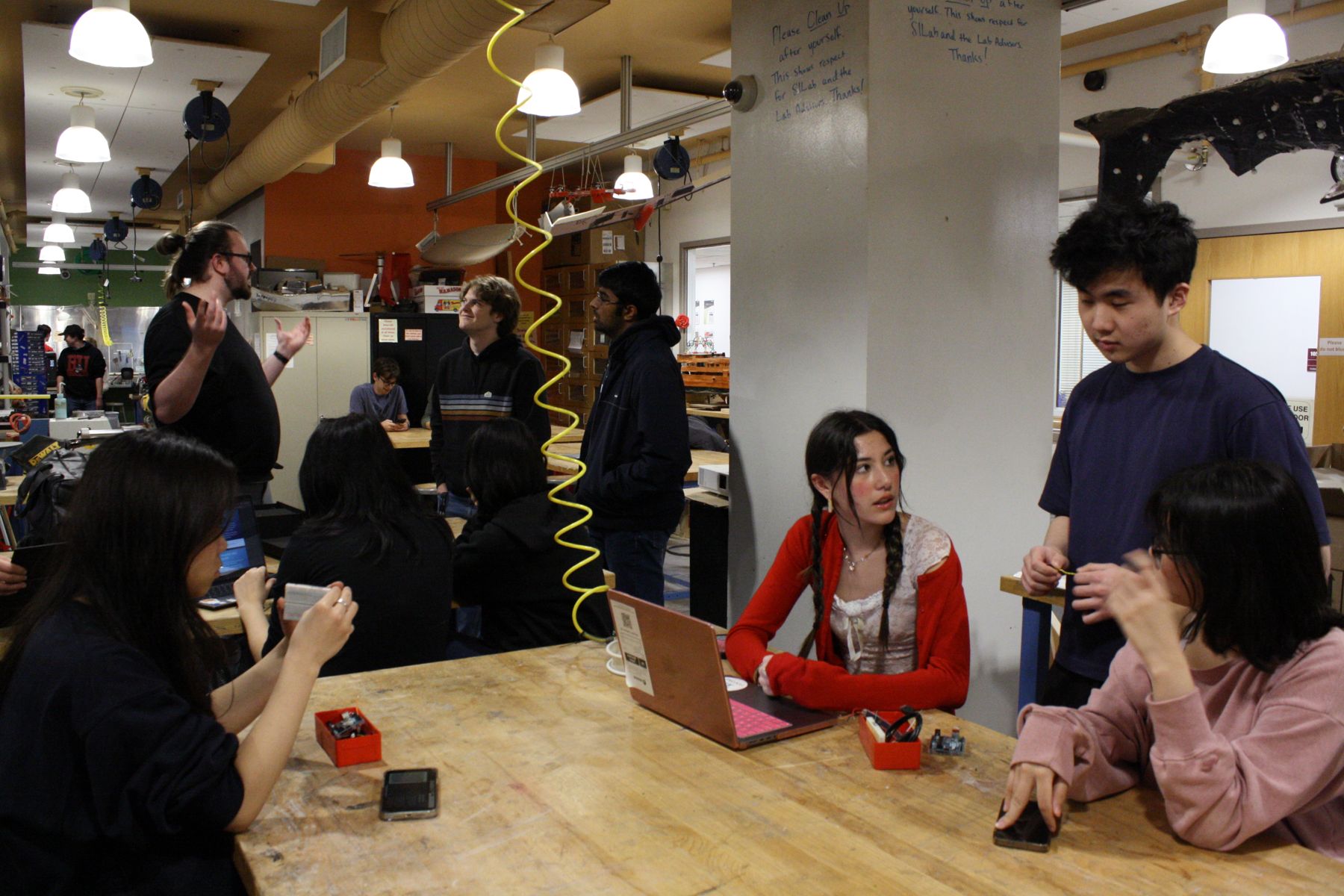 group of students in the foreground discussing ideas and working with electronic components in the foreground, in the background another group is discussing technology with the Lutron rep
